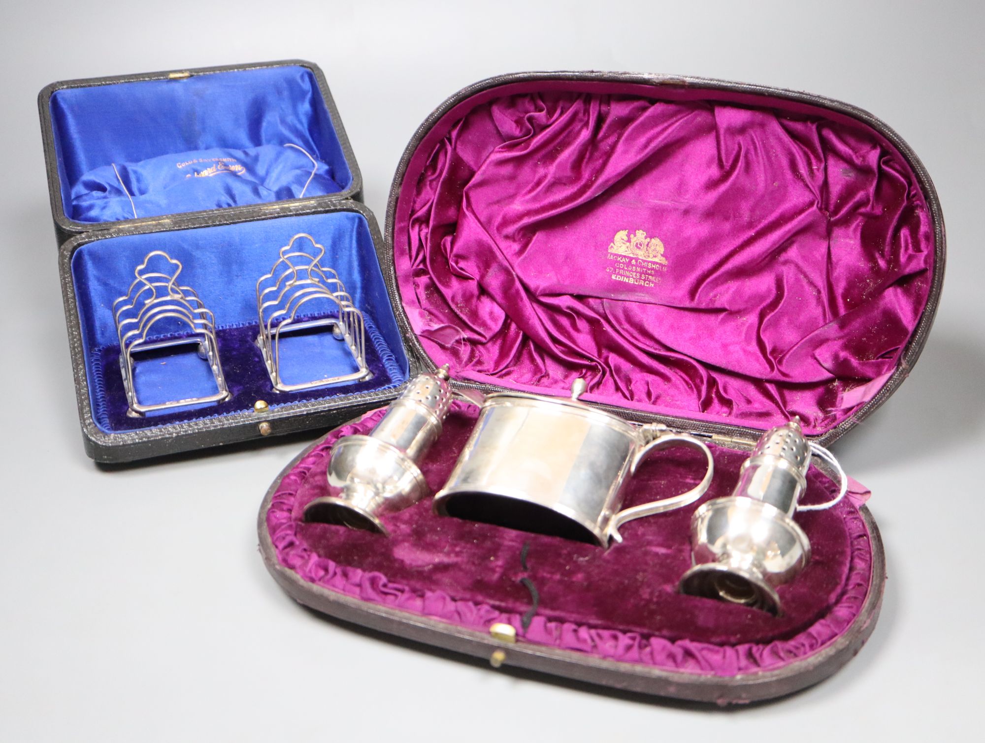 A Victorian silver three-piece condiment set, London, 1882, cased and a pair of small Edwardian silver toast racks, cased.
